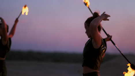 Women-with-fire-at-sunset-on-the-sand-dance-and-show-tricks-against-the-beautiful-sky-in-slow-motion
